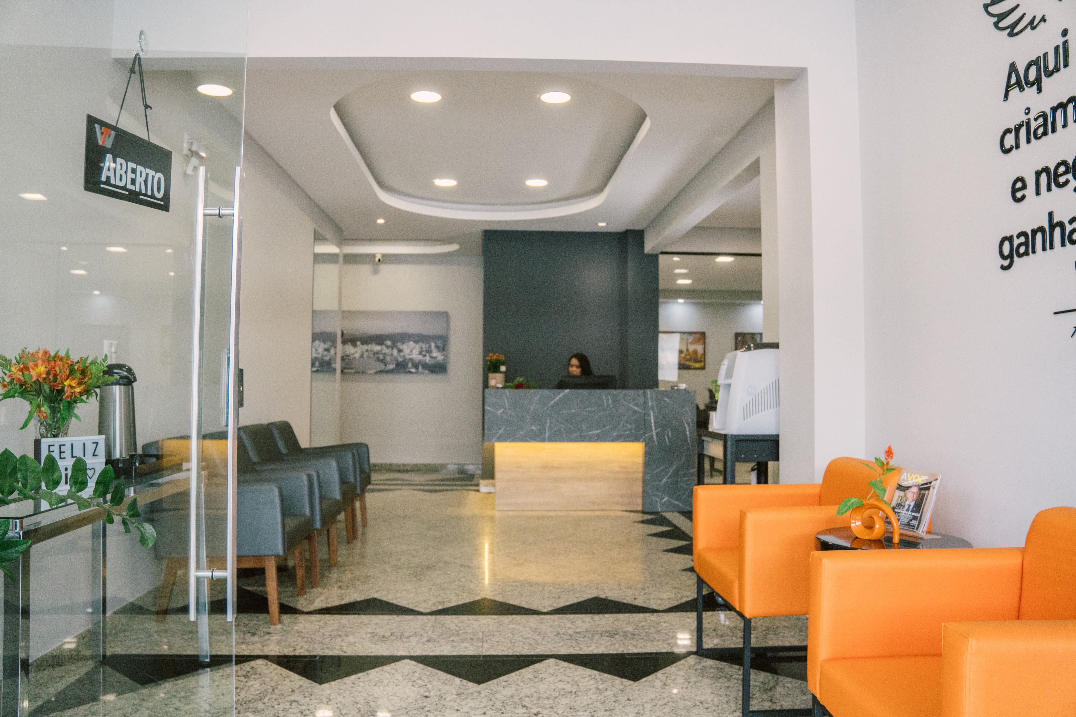 Entrada da Willtay vista da porta de vidro, com recepção, poltronas laranja e área de espera