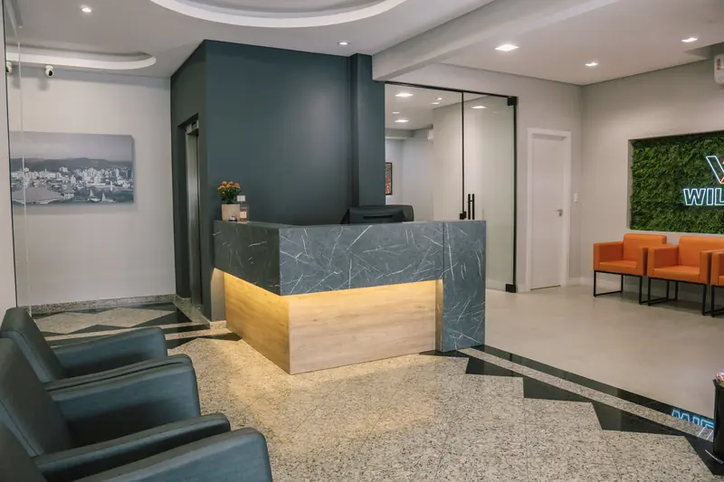 Entrada da Willtay com balcão de recepção, poltronas de espera e acesso ao elevador