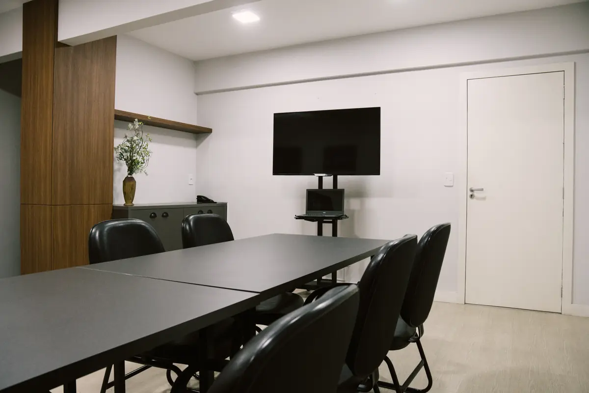 Lado da TV na sala de reunião, com mesa e cadeiras