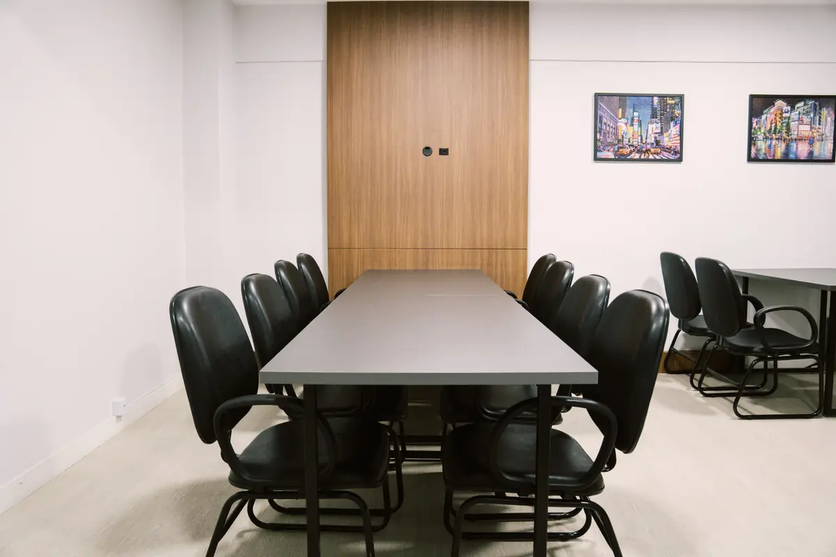 Mesa de reunião vista da cabeceira, com painel de madeira ao fundo